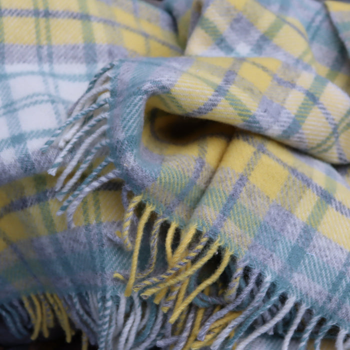 Plaid blanket with yellow, green and blue colors and fringed edges, draped over a stone background. 