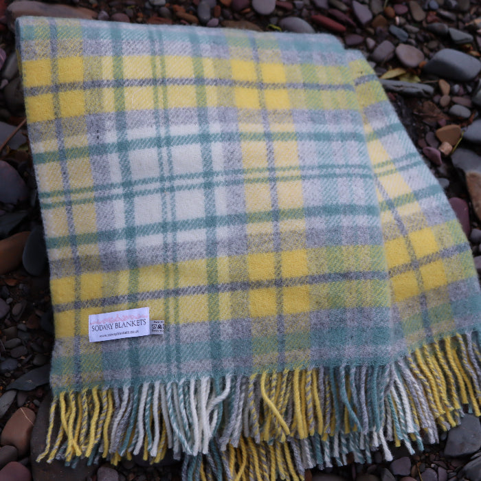 Sea green, yellow, grey and warm white wool blanket with fringes, displaying a 'Solway Blankets' label, placed on a pebbly surface