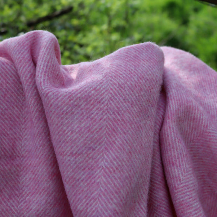 Pale Pink Herringbone Shetland Wool Blanket Throw against a blurred green outdoor background