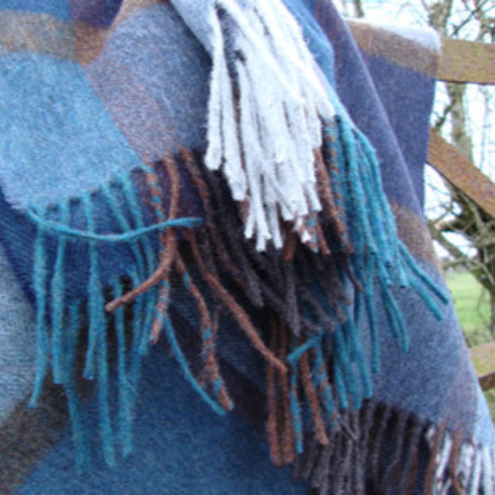 Blue plaid blanket with a colorful fringe draped over wooden gate, outdoors.