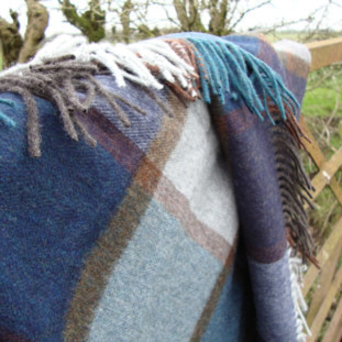 Blue woven blanket with fringe draped over a wooden fence in a natural setting.