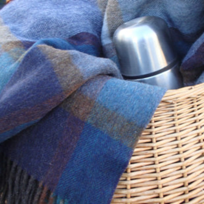 Blue plaid blanket draped over a woven basket with a silver thermos inside