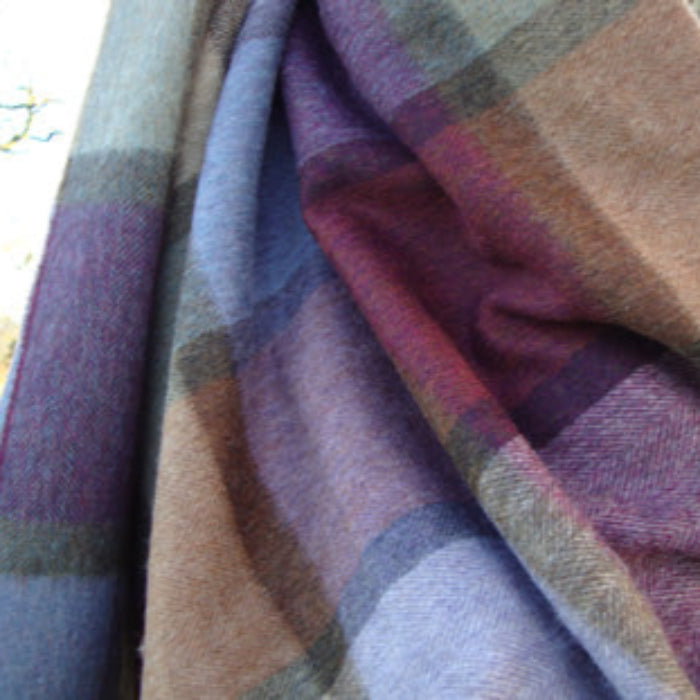 Plaid fabric blanket with purple, brown, and green colors draped over a surface.