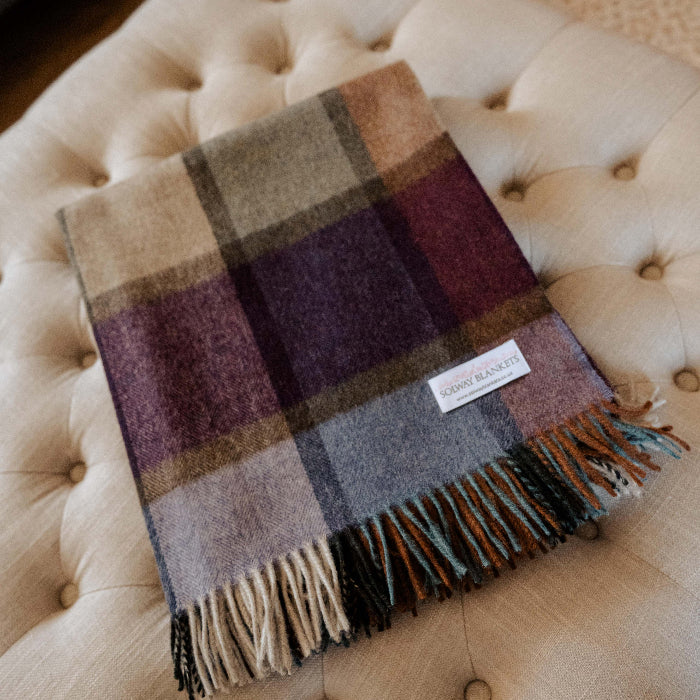 Country style colorful plaid blanket with fringe neatly folded on beige ottoman