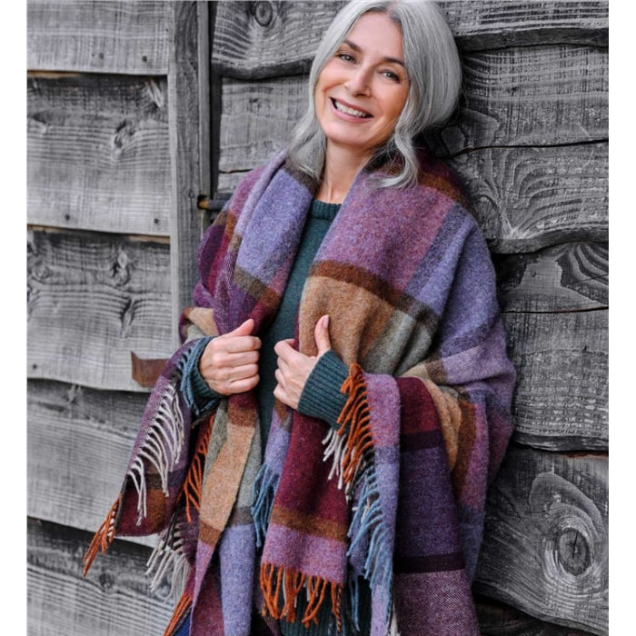 Woman with a colorful plaid blanket draped over shoulders against a wooden building.