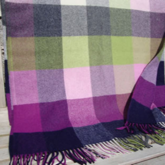 Plaid throw with a purple, pink, green, navy blue and white pattern draped over a wooden bench outdoors