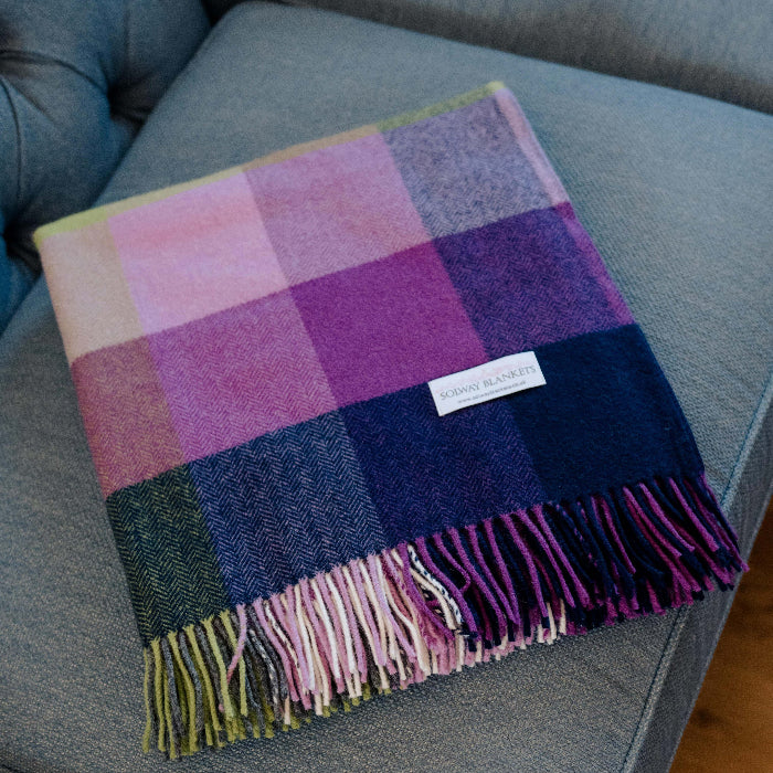 Colorful plaid throw with fringes folded neatly on a grey couch