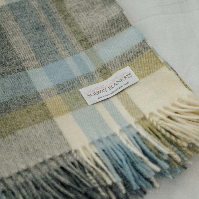 Plaid duck egg blue, grey and green blanket throw with fringes and a visible Solway Blankets label on a light background