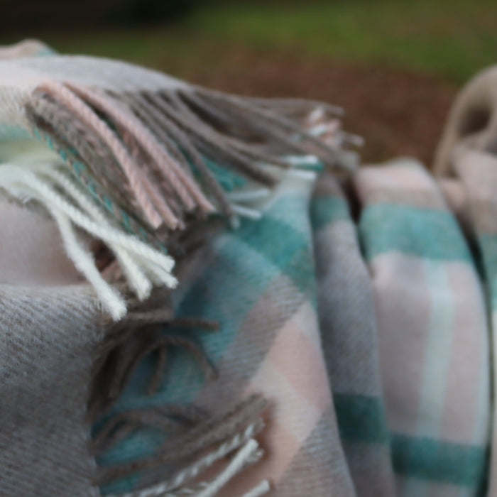 Close up of a plaid blanket with fringes in cream, beige, pink and jade colors.