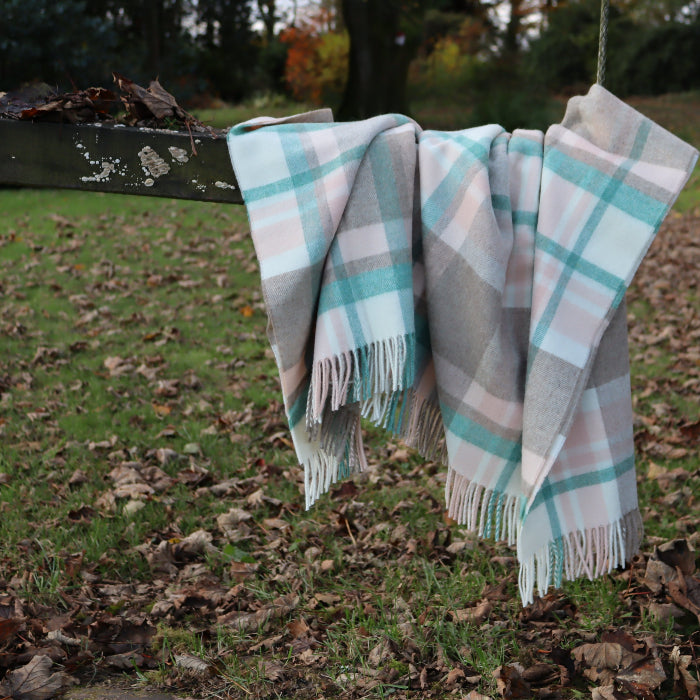 Plaid blanket throw with fringe draped over a wooden swing in a natural setting with grass and leaves.