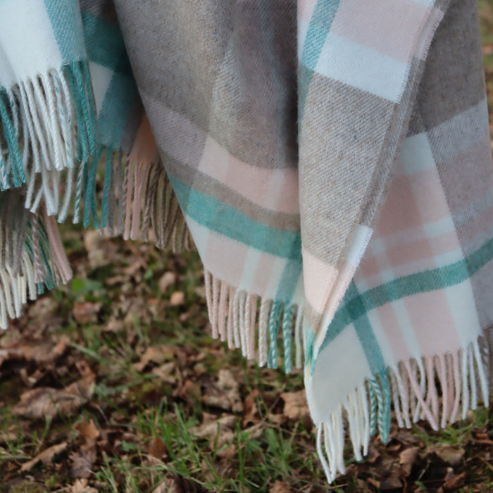 Plaid cream, beige, soft pink and muted jade blanket  throw with fringes on a grassy ground with leaves