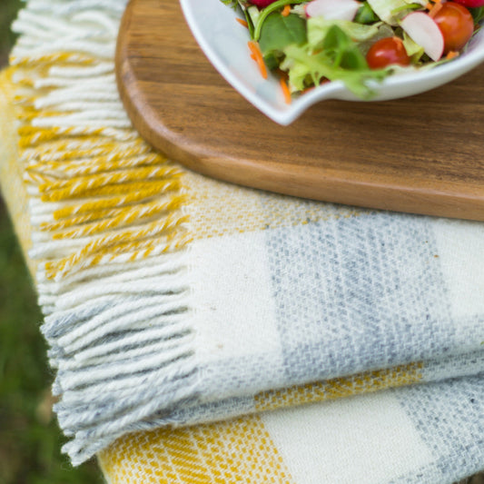 Yellow and grey check wool blanket folded underneath a wooden table with a salad bowl
