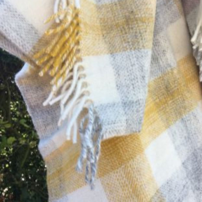 Close up of a plaid blanket with yellow and grey pattern with fringe, on a blurred natural background