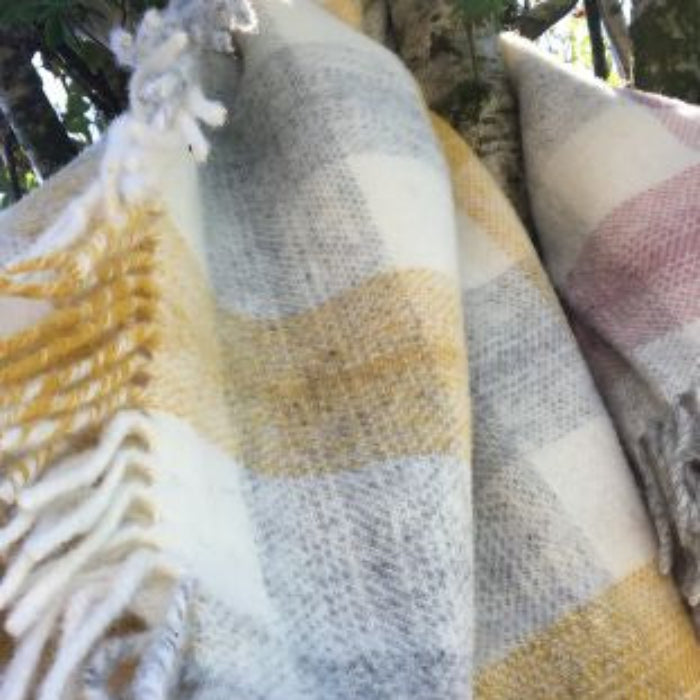 Plaid yellow, grey and white wool blanket outdoors draped around a tree branch.