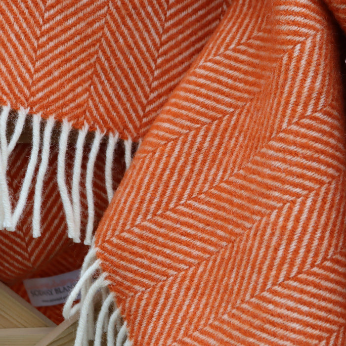 Pumpkin orange and white fishbone wool patterned blanket with fringes on a wooden surface.