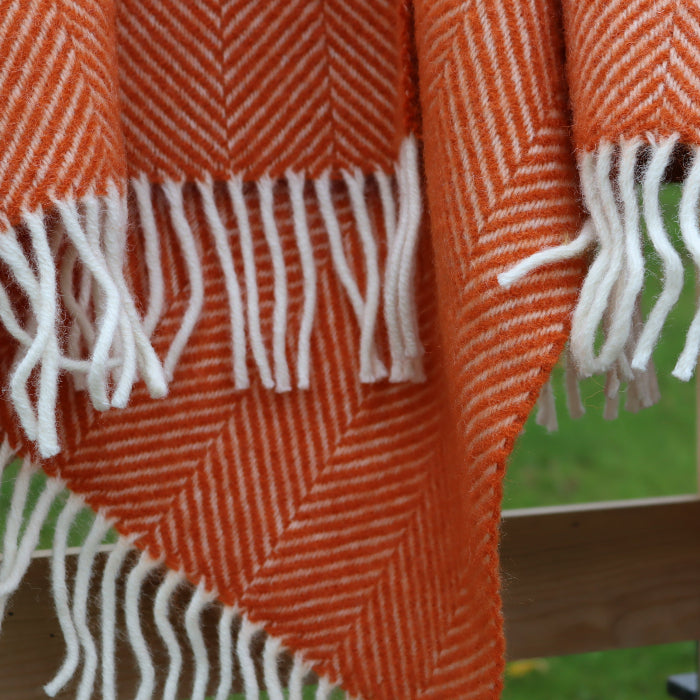 Pumpkin orange fishbone style wool blanket with white fringe draped over a wooden fence.