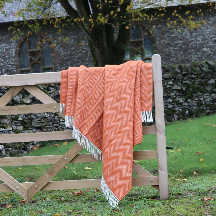 Pumpkin orange wool blanket with white fringe draped over a wooden gate in a rural setting.