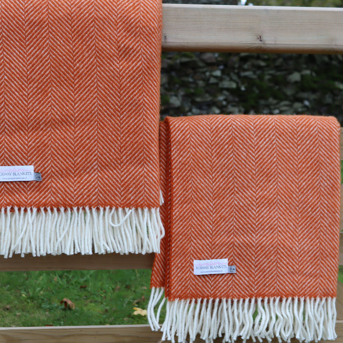Two pumpkin orange fishbone style wool blankets with white fringes, displaying a Solway Blankets label, folded over a wooden fence.