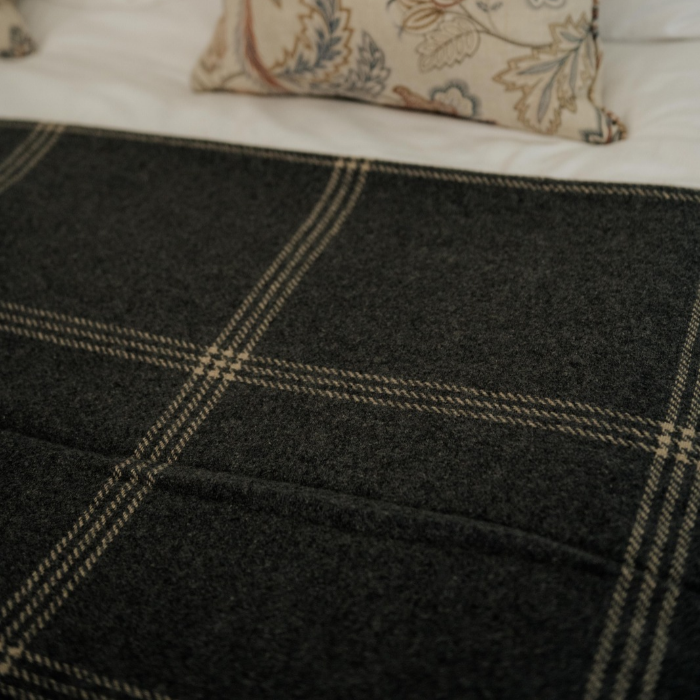 Close-up of fine ivory overcheck woven into blue grey luxury cashmere blanket, styled on a bed with a floral pillow in the background.