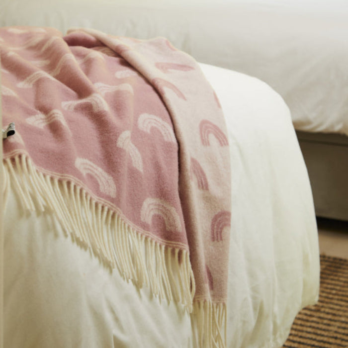 Rainbow Pink Merino Wool Baby Blanket with white rainbow patterns draped over a bed in a bedroom setting.