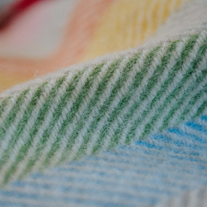 Close up of a rainbow coloured wool blanket highlighting the green and blue patterns