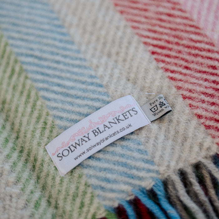 Close up of a colourful rainbow style wool blanket with a 'Solway Blankets' label