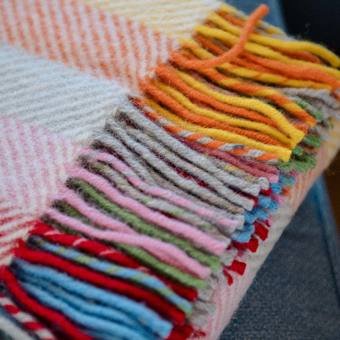 Rainbow coloured herringbone wool blanket with colourful fringe on blue couch
