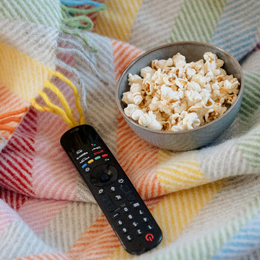 Vibrant rainbow coloured wool blanket underneath a bowl of popcorn and remote control 
