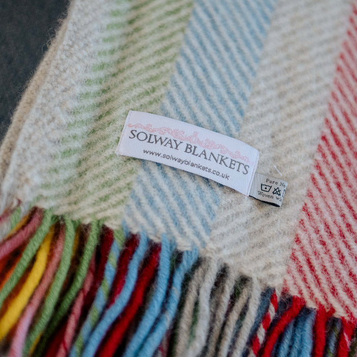 Multicoloured rainbow style wool blanket with colourful fringe, featuring a Solway Blankets label.