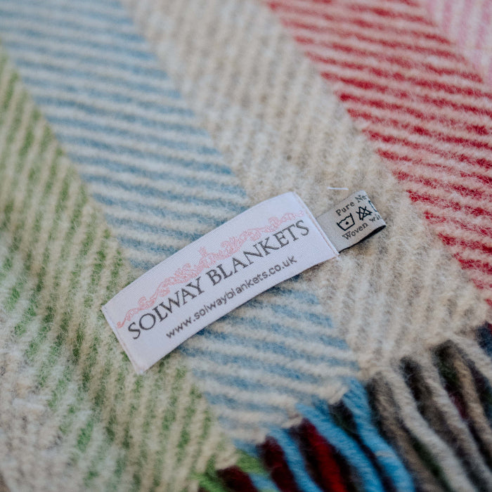 Close up of a colourful rainbow stripe wool knee blanket with a 'Solway Blankets' label 