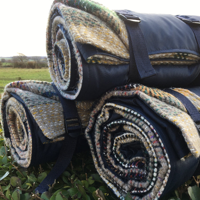 Three rolled up blankets made from recycled materials with patterned fabric stacked on top of one another in a field