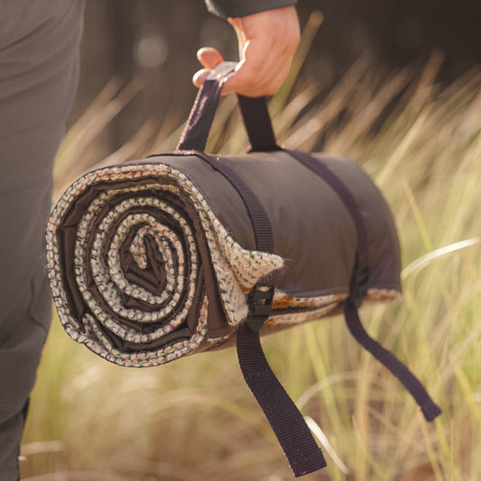 Person holding a rolled-up blanket made from recycled materials with decorative patterns in a natural setting