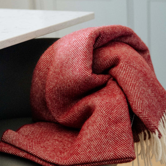 Red Herringbone Shetland Wool Blanket draped over a chair in a room with a table and white walls.