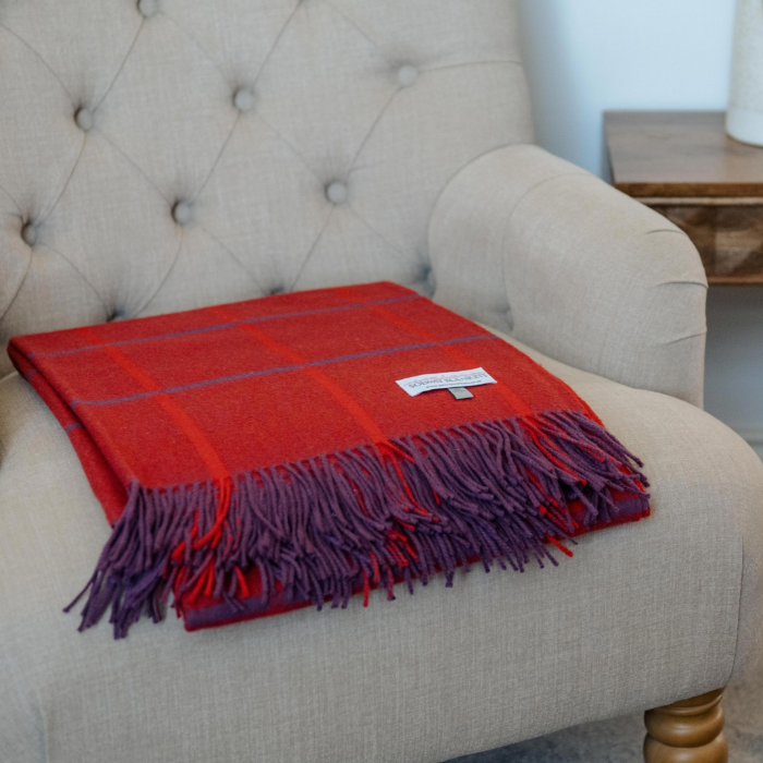 Pure cashmere throw in rich red and purple windowpane check with twisted fringe, neatly folded on a neutral linen covered arm chair