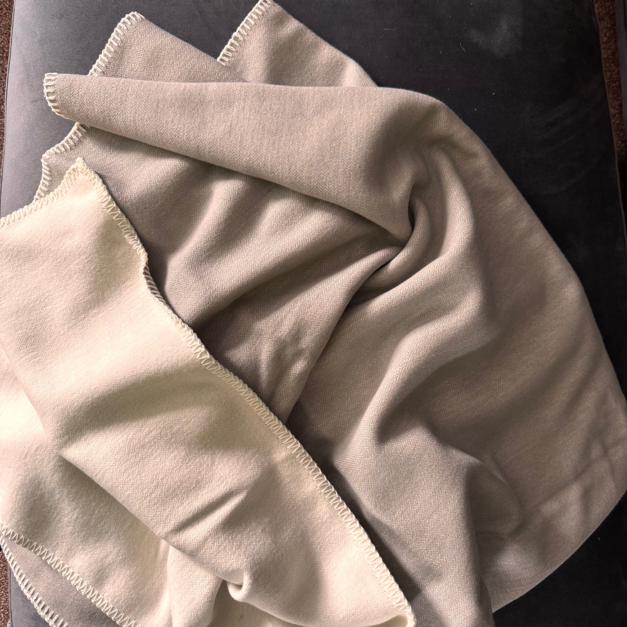 A folded light grey cotton throw with visible stitched edges, draped on a dark textured surface.
