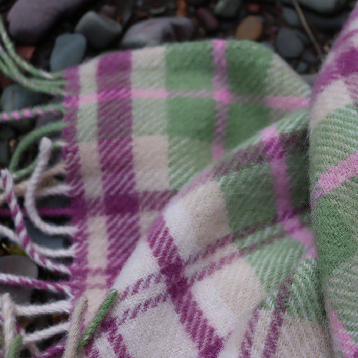 Close up of a plaid woollen blanket with purple and green patterns on a textured background.