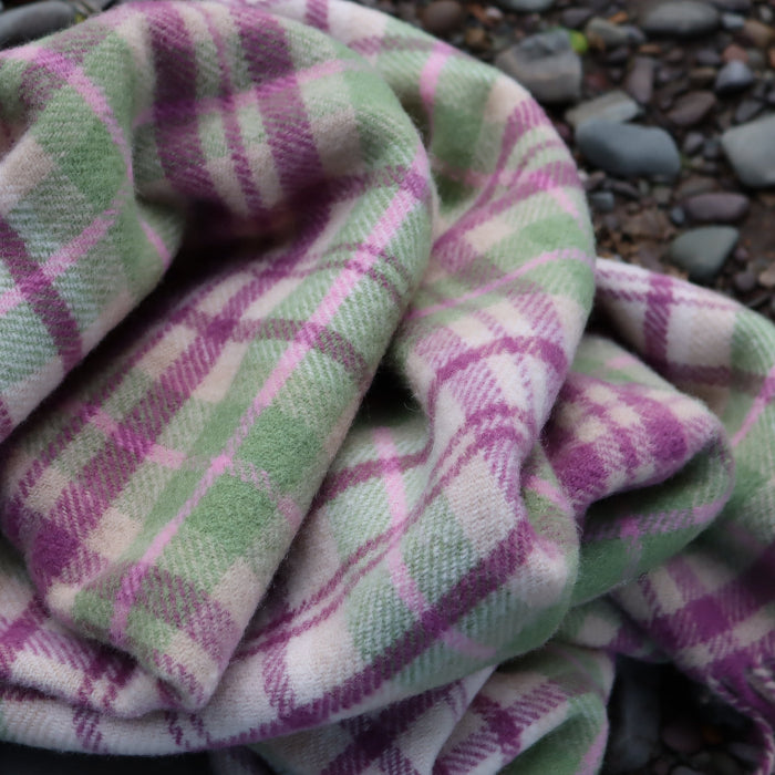 Colourful check wool blanket, with colours of pink, magenta, green and cream with fringe, draped over a stone background