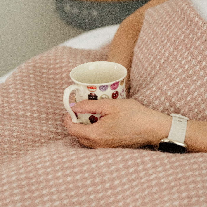 Person holding a mug wrapped in a rose coloured waffle textured blanket throw.