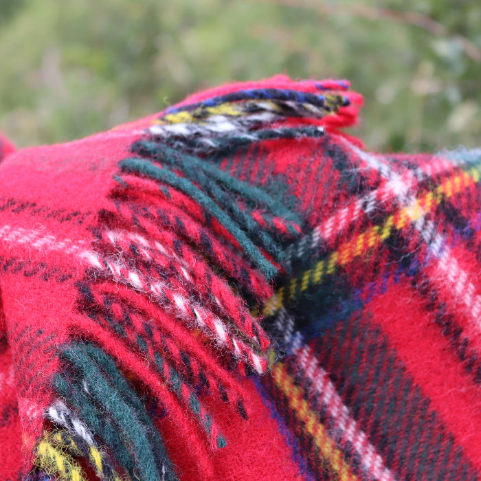 Close up of a red woolen tartan blanket with accents of black, blue, white and yellow with fringe, outdoors.