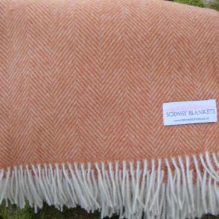 Saffron herringbone throw with a white fringe and a 'Solway Blankets' label folded over fence outdoors