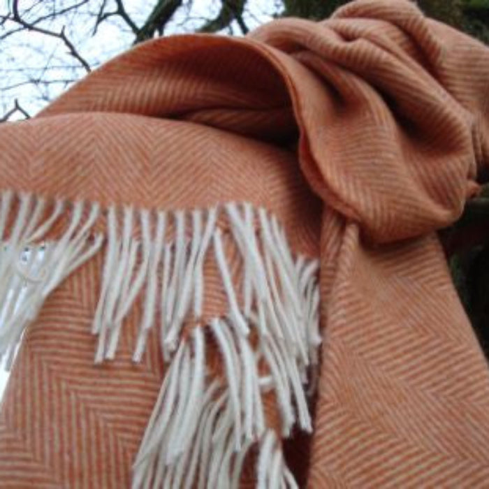 Saffron herringbone throw with white fringe draped over a branch against a natural background