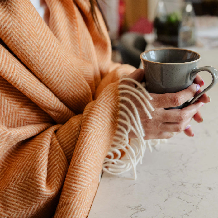 Person wrapped in a warm saffron orange throw holding a mug over a marble surface
