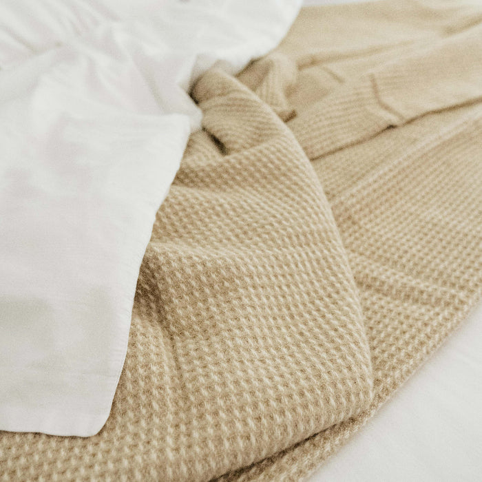 Close up of a sandstone beige waffle textured throw wrapped in a white duvet on a bed