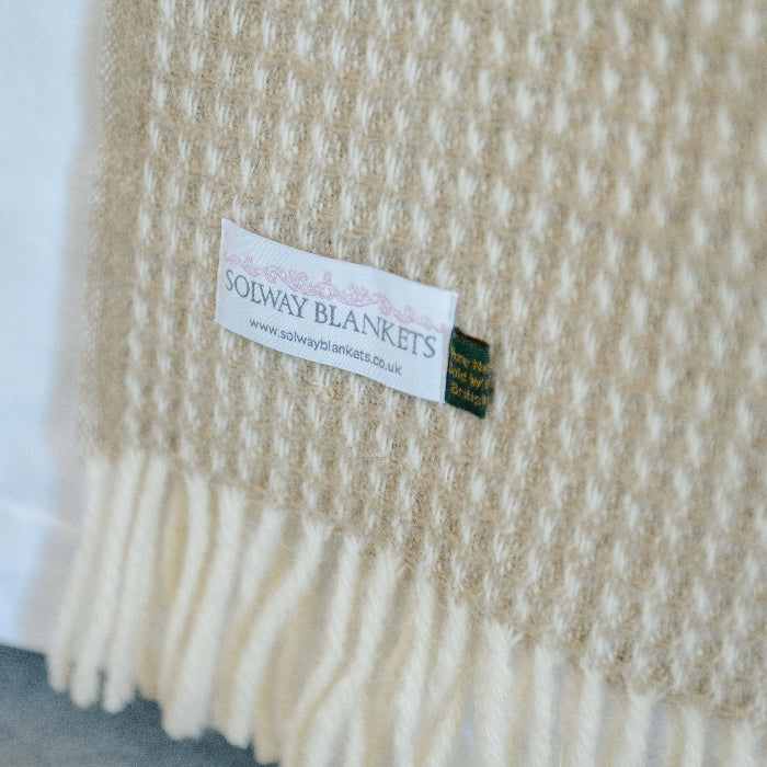 Close up of a sandstone beige waffle textured wool throw with a visible Solway Blankets label on a white background