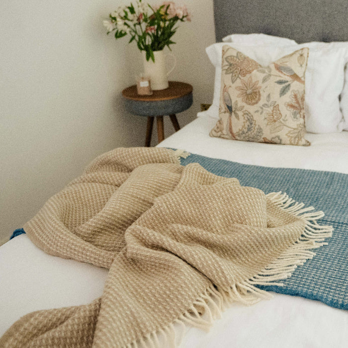 Bed with sandstone beige waffle textured blanket on top and floral pillows in a bedroom setting.