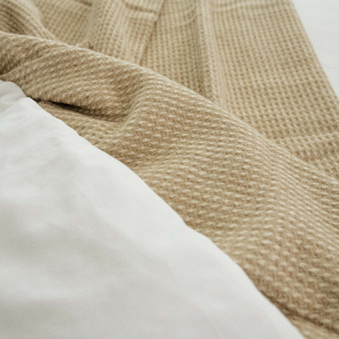 Close up of a sandstone beige waffle textured throw on a white bed 