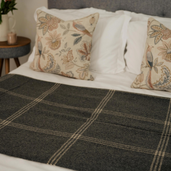 Luxury blue grey Scottish cashmere blanket with fine off-white overcheck and fringed edge, styled over bed with decorative cushions