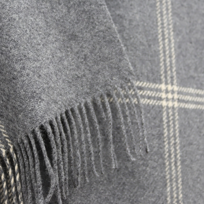 Close-up of fine ivory overcheck woven into a grey cashmere blanket with fringed edges and a subtle cream plaid pattern.