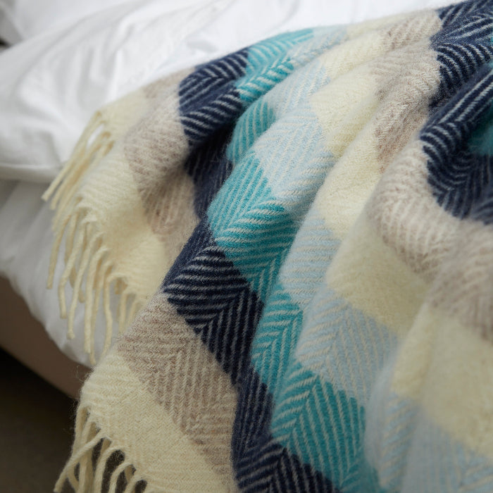 Colours of the sea - different shades of blue in a patterned wool blanket with fringes, draped over white bedding