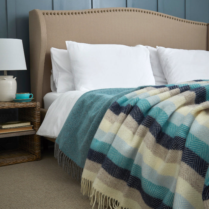 Bedroom with a bed featuring a colourful striped blanket in shades of blue, nightstand with lamp, and blue paneled wall.